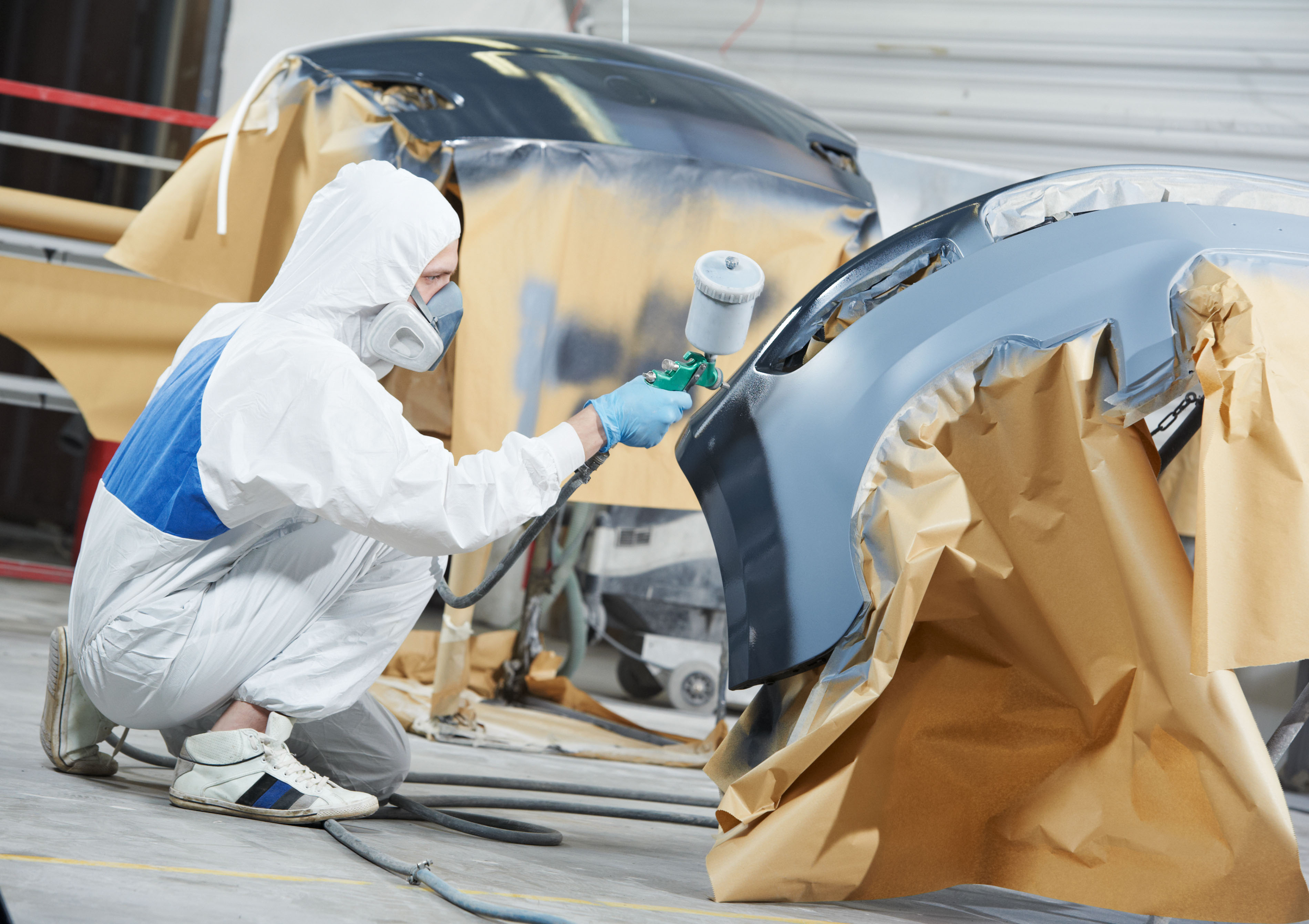 An image of an Auto Mechanic Worker spraying painting various car pieces.