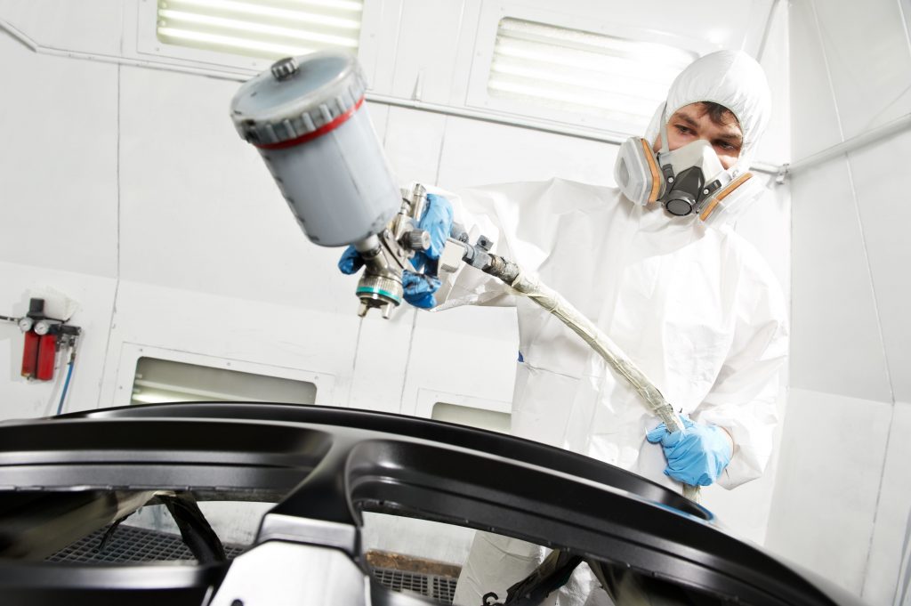 An image of an Auto Mechanic painting a car bumper